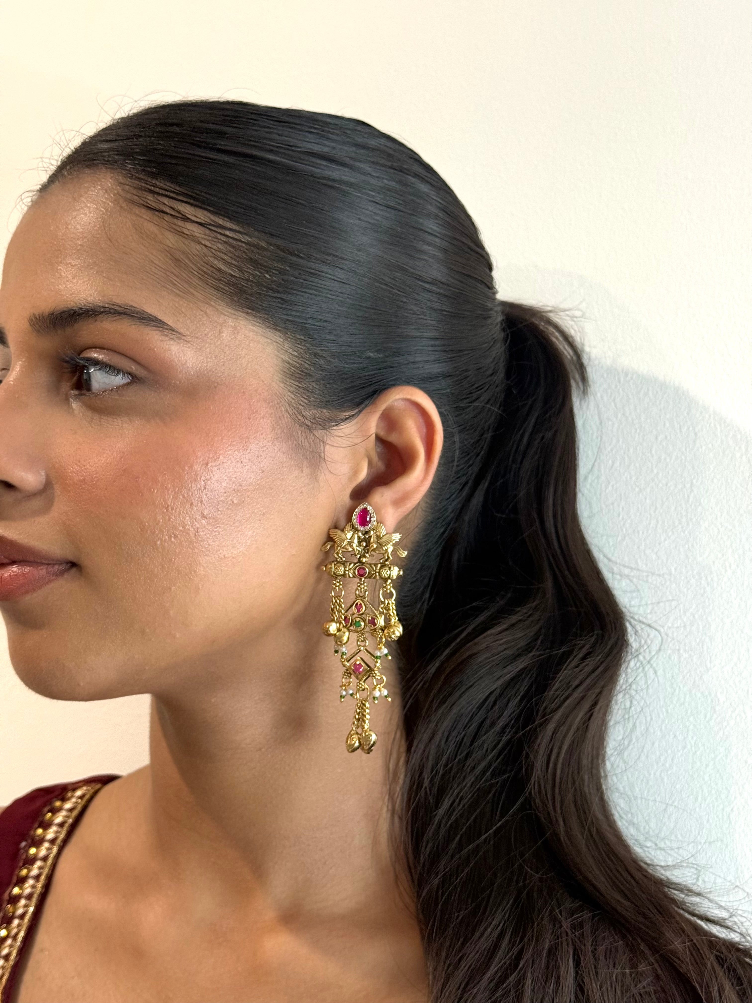 Woman wearing gold earrings with a red gemstone against a neutral background