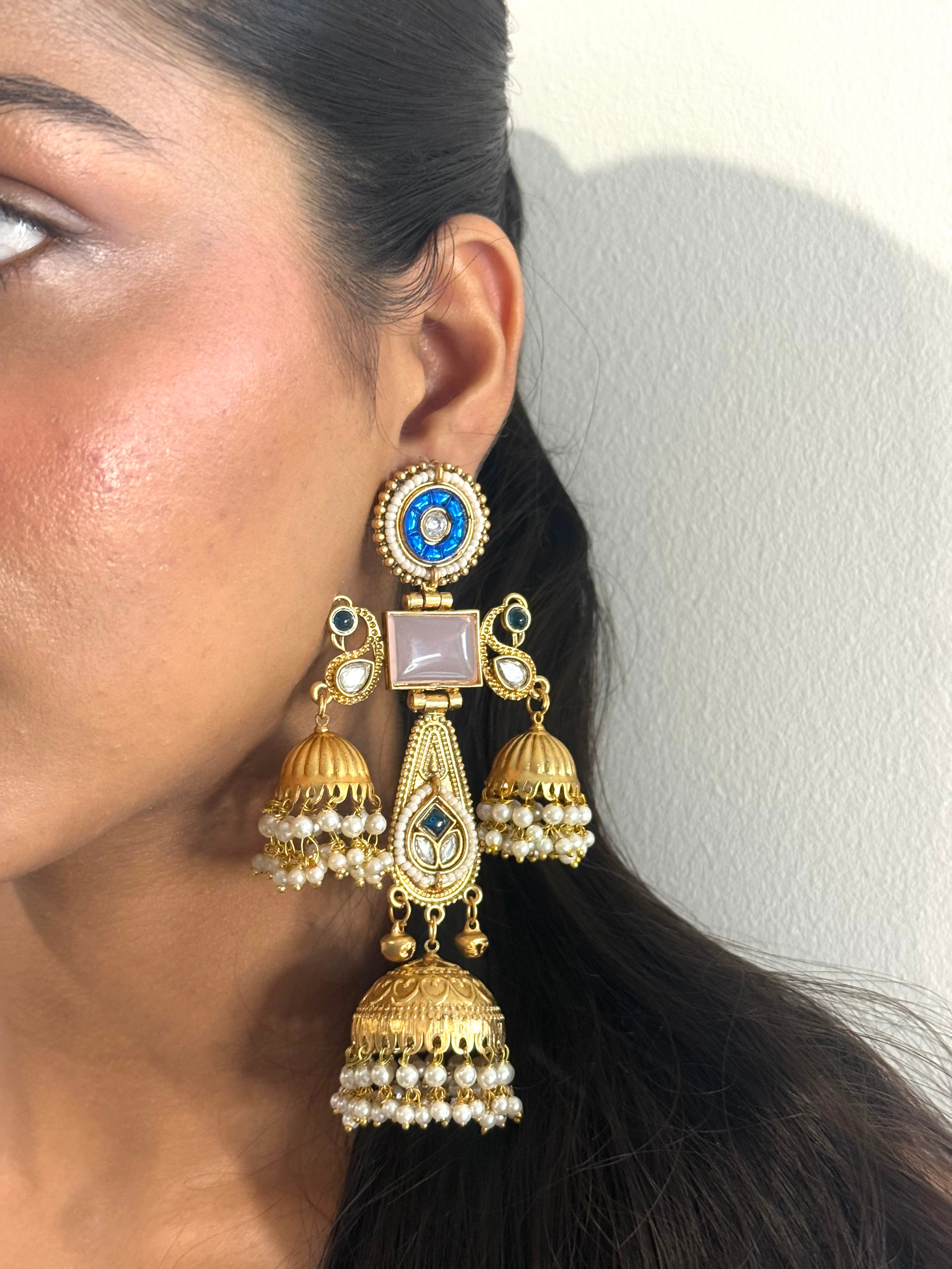 Close-up of a person wearing gold and pearl earrings with a neutral background