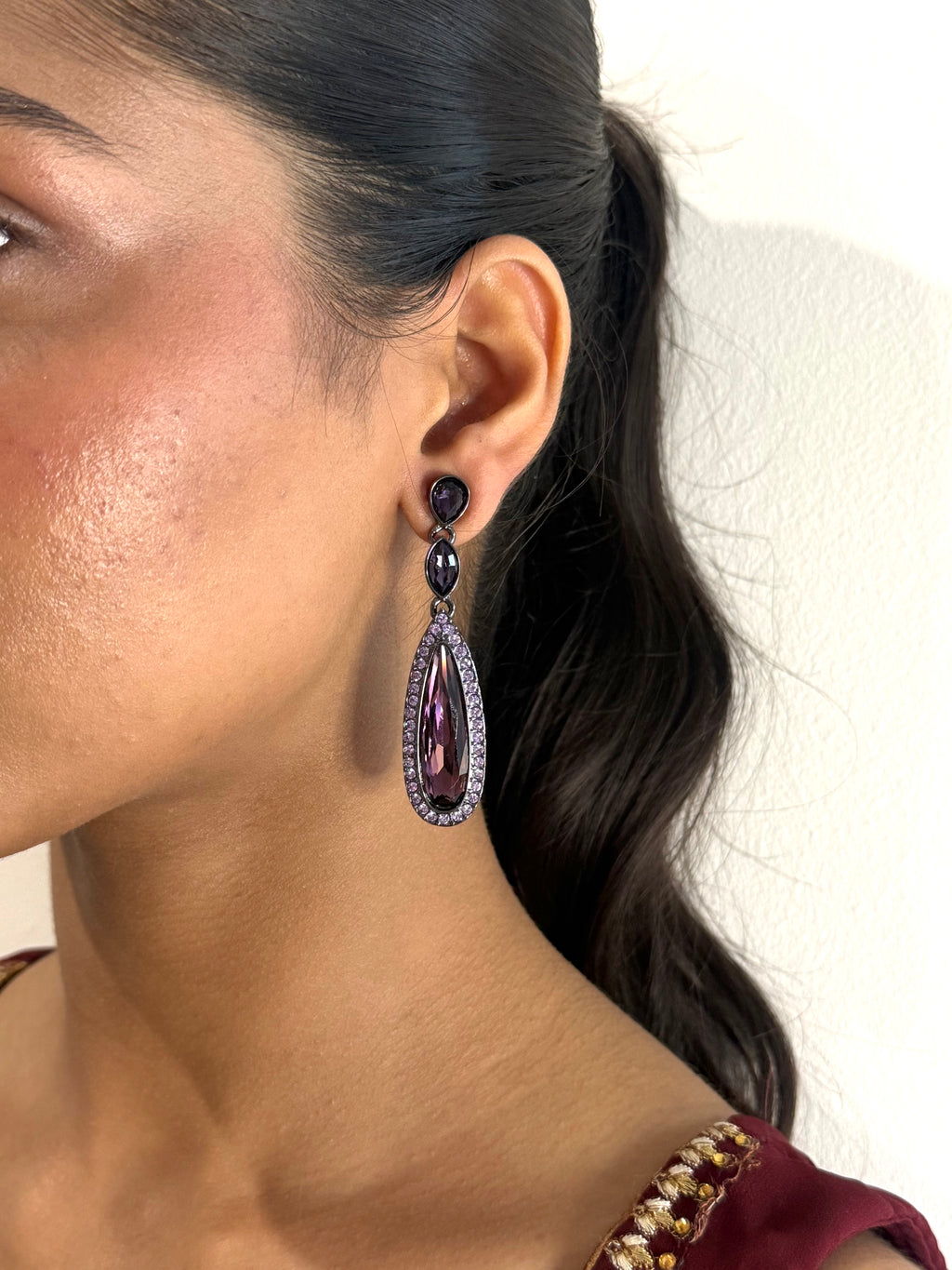 Close-up of a woman wearing a purple teardrop earring with a black gemstone on a plain background. 