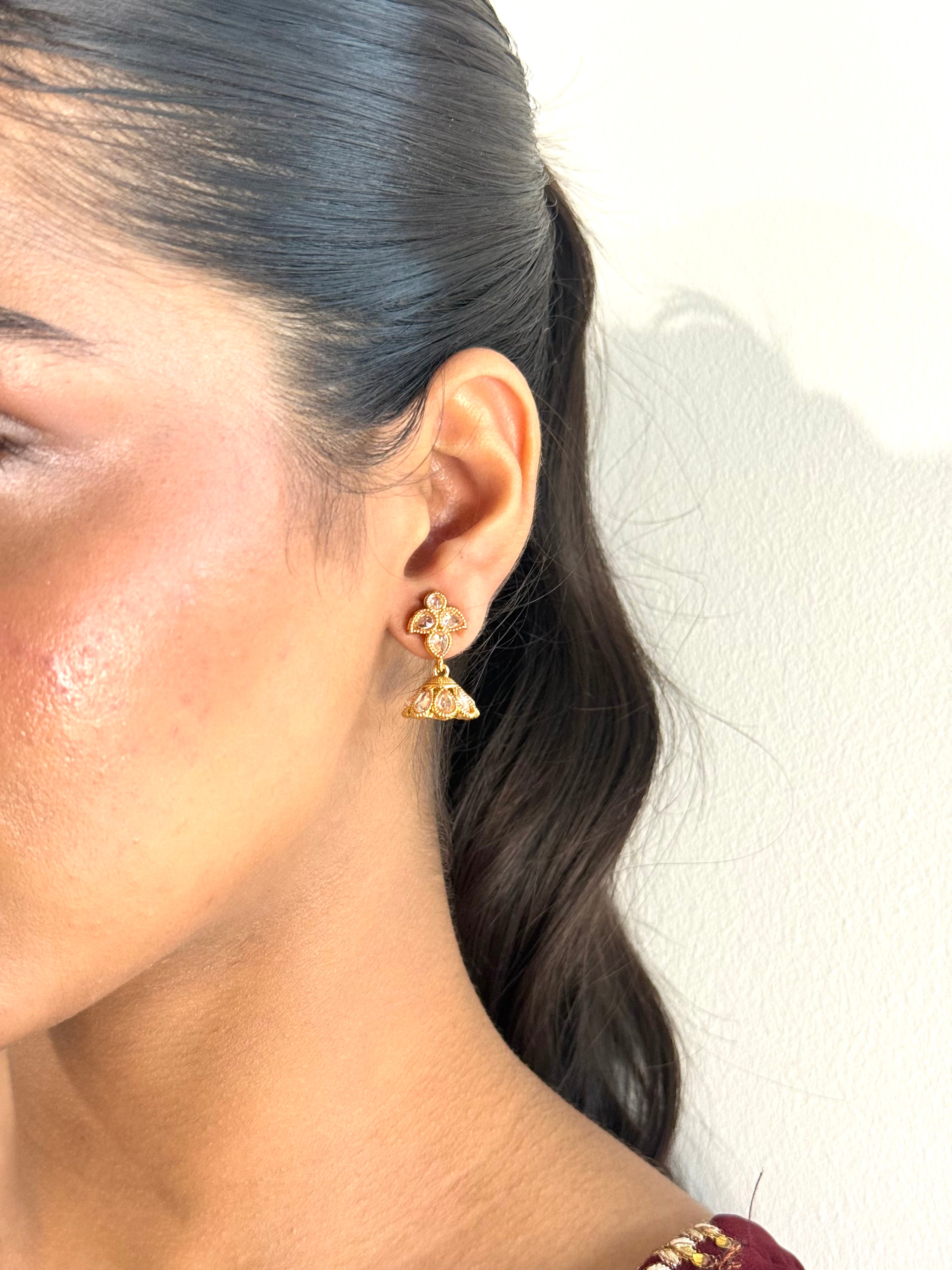Close-up of a person wearing gold triangle earrings with a neutral background
